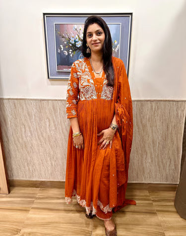 Woman in an orange dress standing indoors with a painting on the wall.